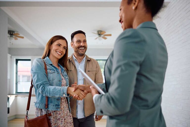 A young couple reviewing a home floor plan with documents and keys on a wooden table.